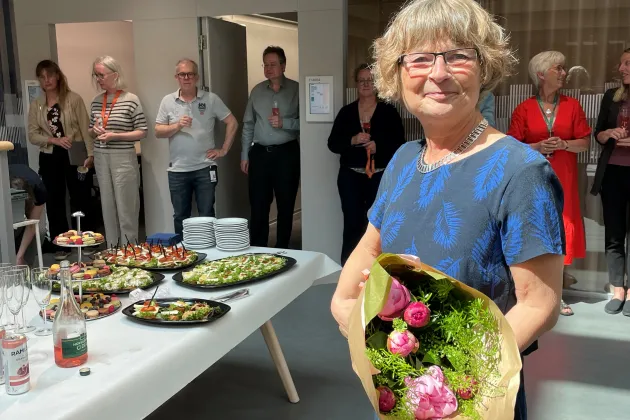 Kvinna med blomsterbukett i handen och kollegor vid mingelbuffé