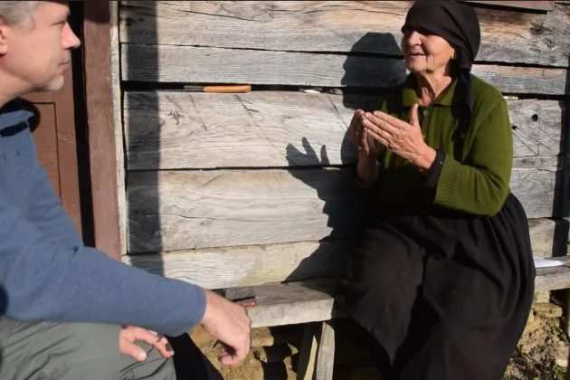 Man intervjuar äldre kvinna på en träbänk