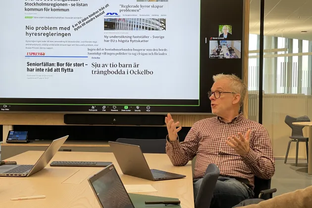 Man sitter vid konferensbord med presentation på skärm bakom sig